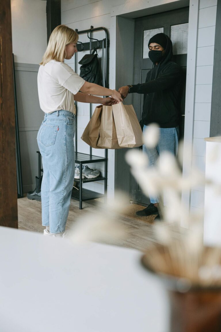 A woman receives a delivery package from a courier at her doorstep inside a modern home.