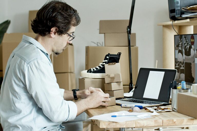 Businessman packing products and managing an online store from his desk with a laptop.